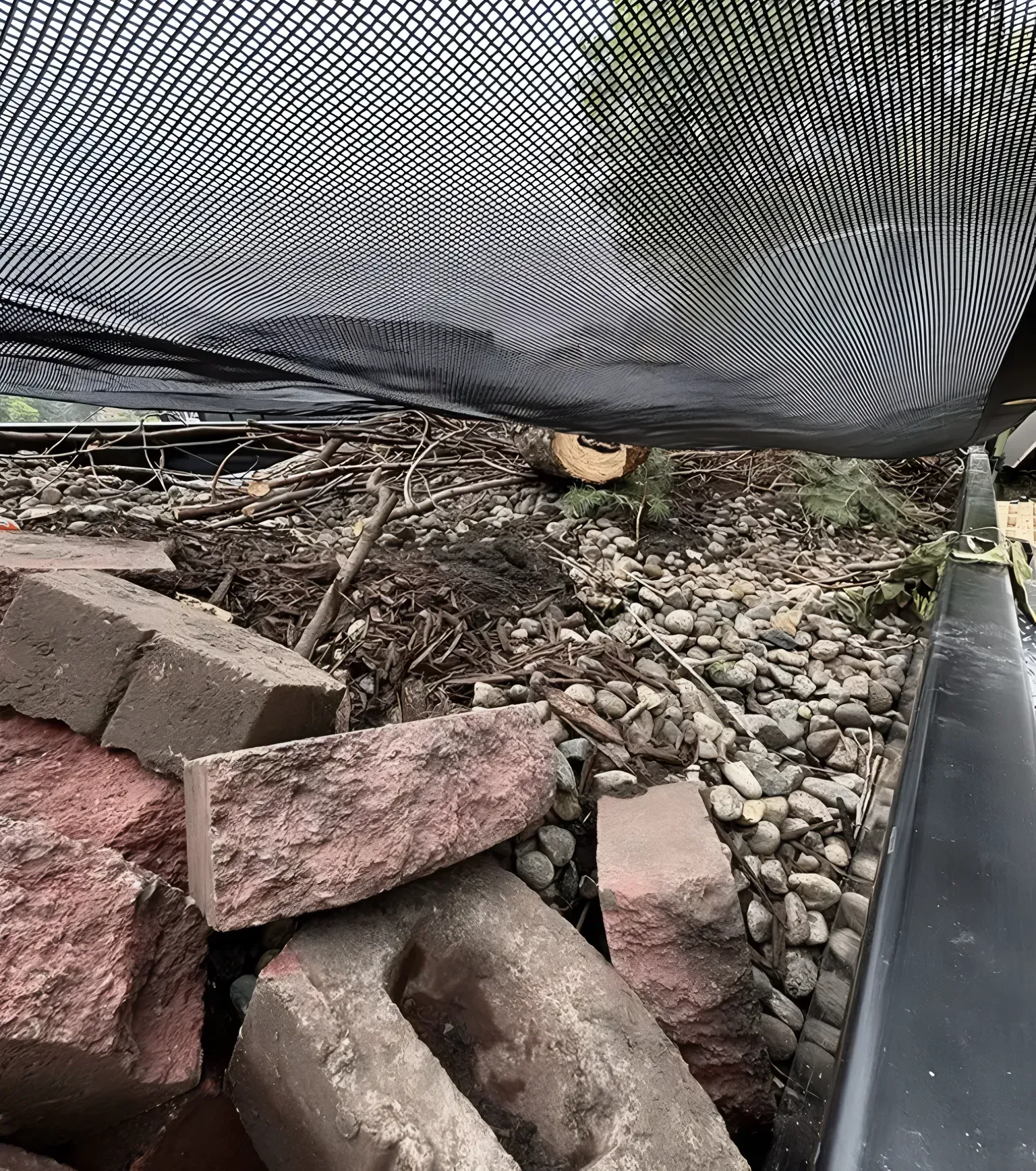 A truck bed filled with bricks, rocks, and debris, viewed from below a black mesh.