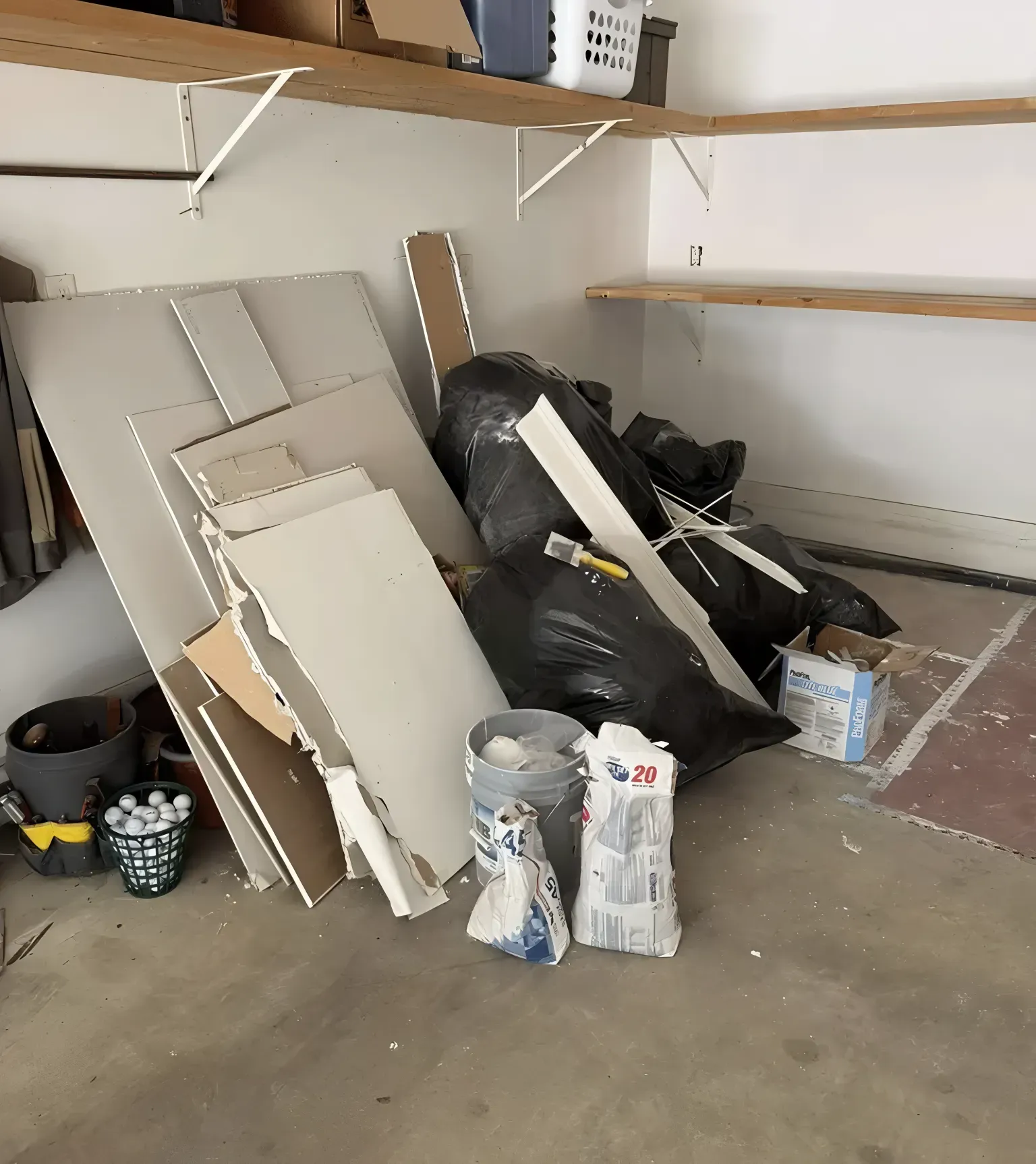 Garage with construction debris, bags, drywall, buckets, and shelves.