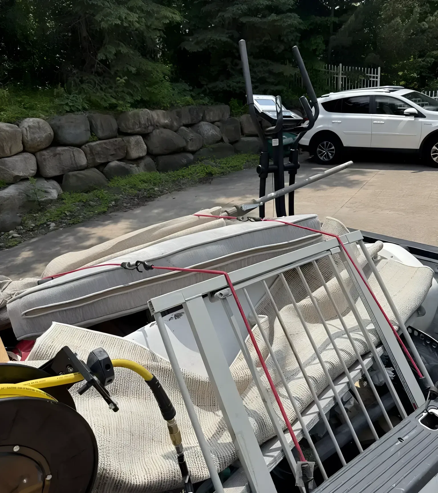 A truck bed filled with various discarded items, including exercise equipment, a mattress, and a metal gate.