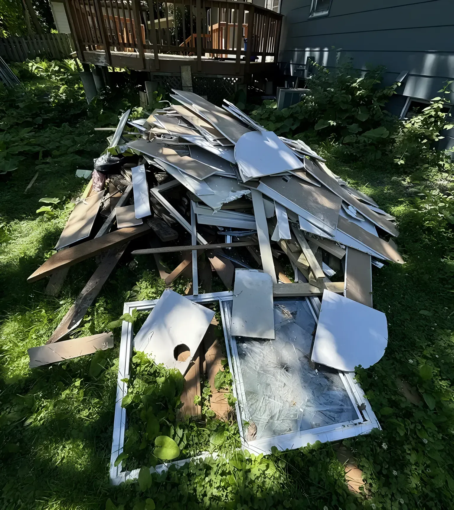 Pile of construction debris, including wood and a window, lying on green grass.