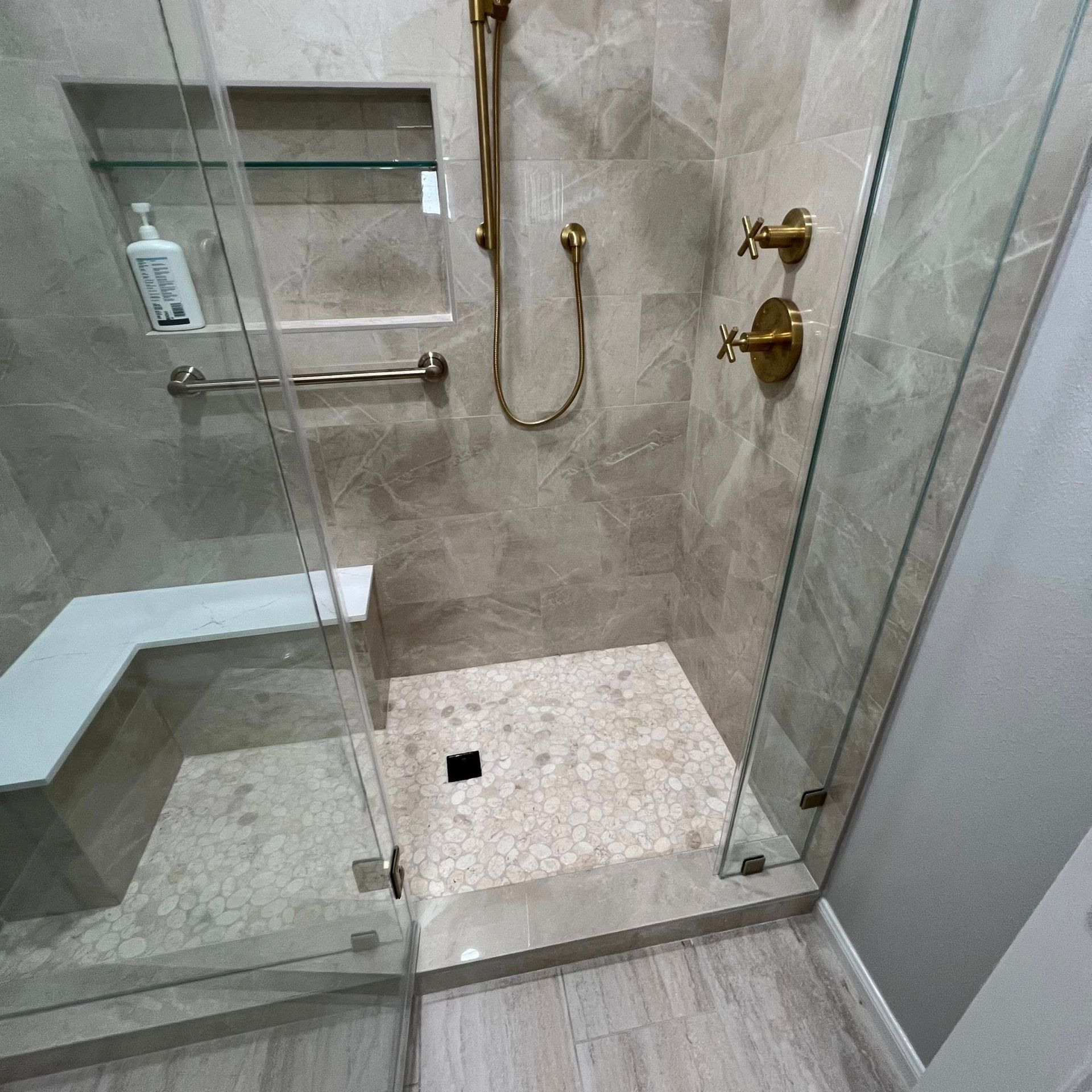 A modern walk-in shower with stone tile walls, a glass door, a built-in bench, and gold-toned shower fixtures.