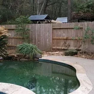 A swimming pool with a wooden fence and a picnic table in the background.