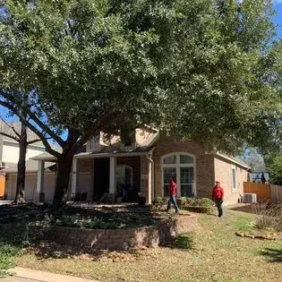 A man is standing in front of a house with a large tree in front of it.