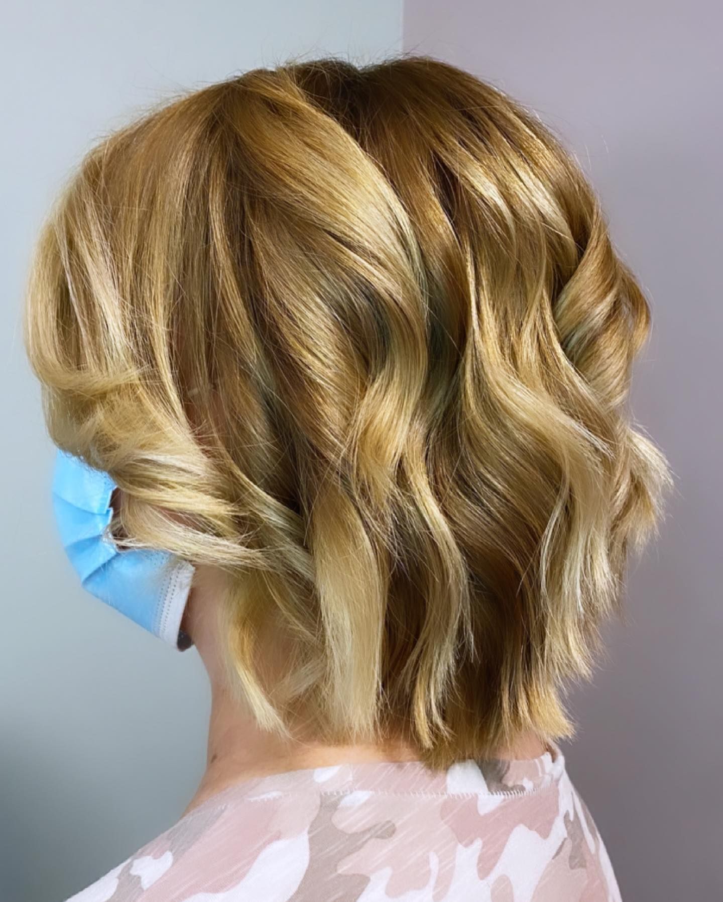 Woman with blonde, wavy bob haircut wearing a blue face mask.