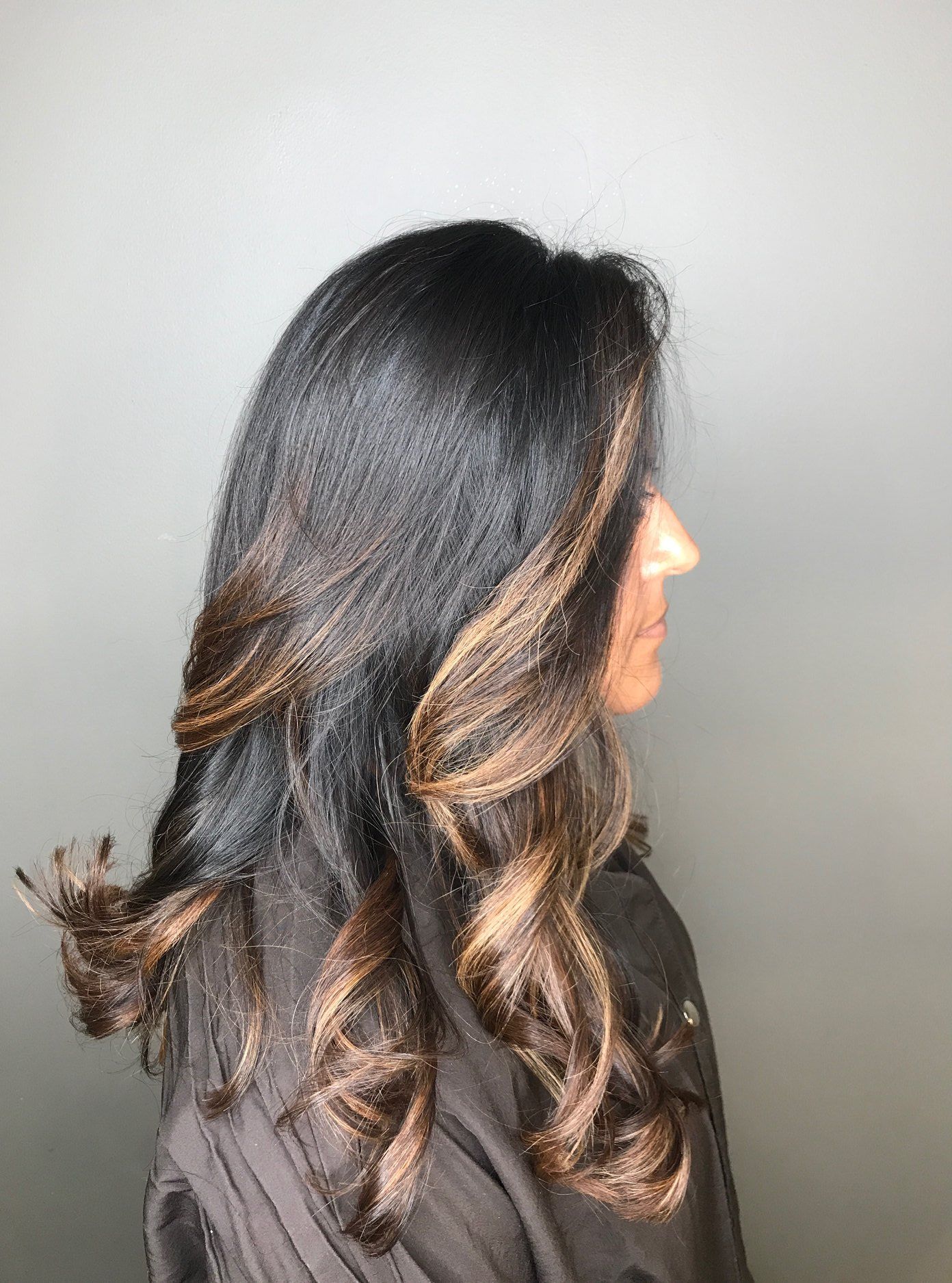 Woman with dark hair and brown highlights, styled in loose curls.