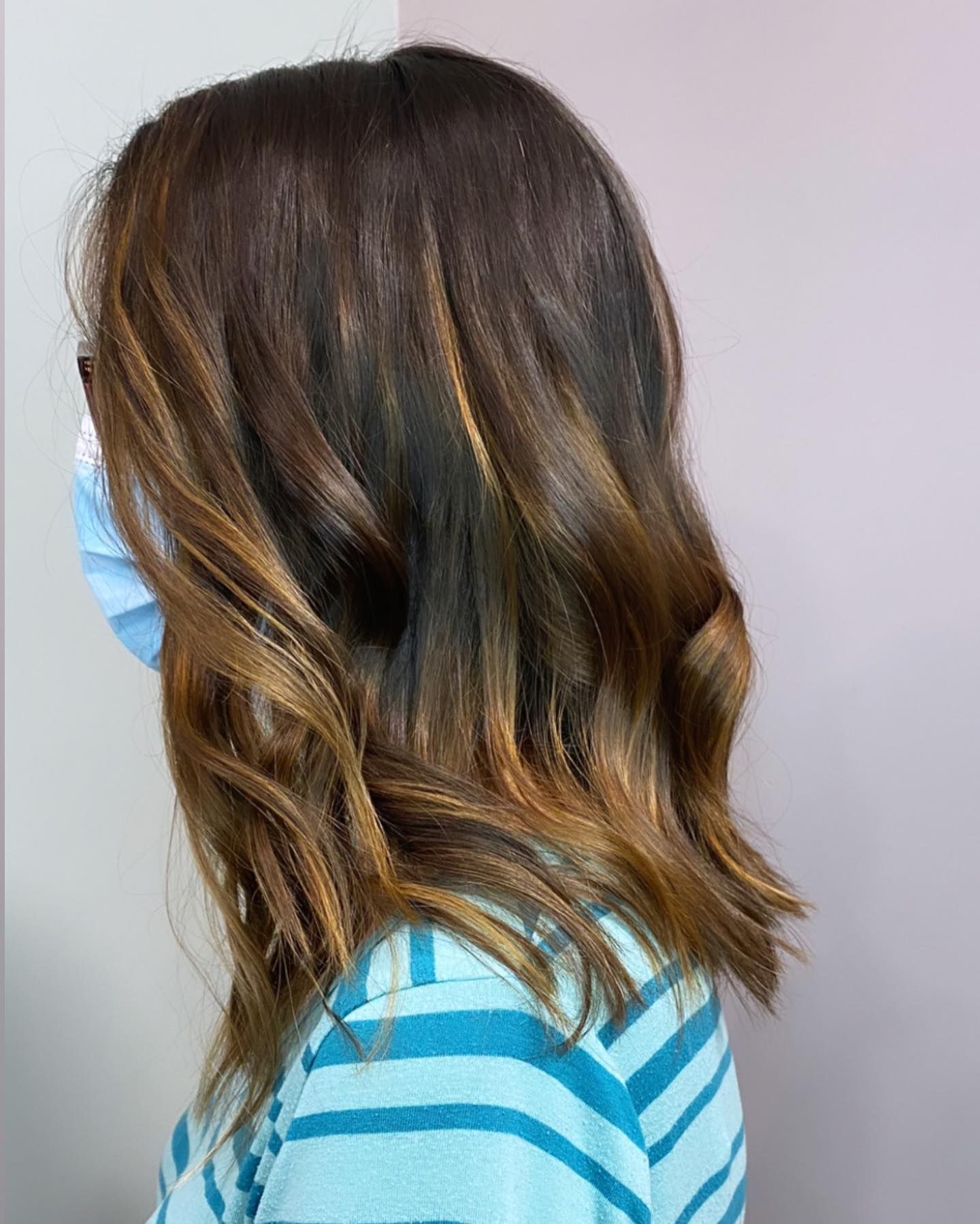 Woman with wavy brown hair and face mask; hair is highlighted with golden brown.