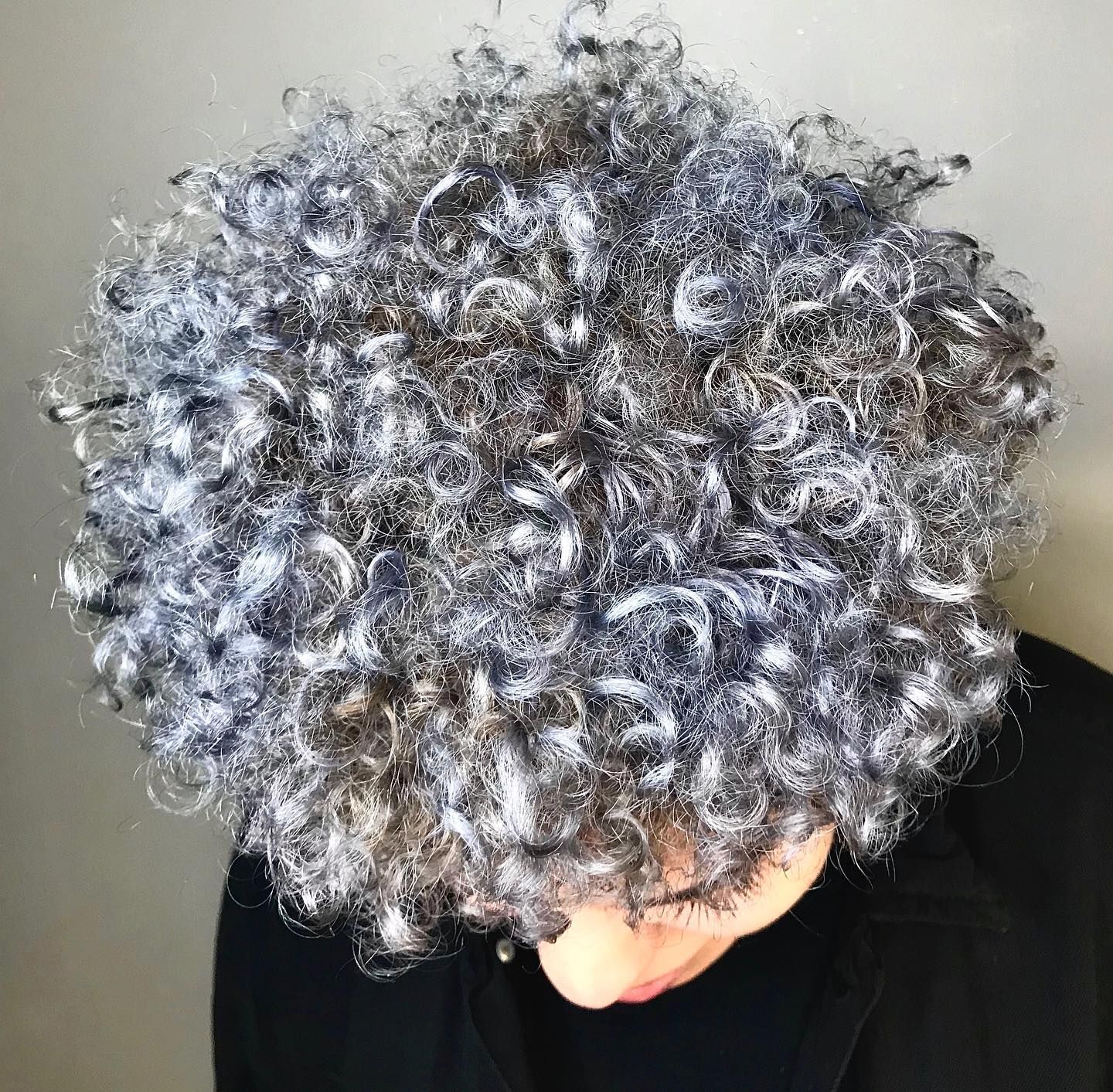 Person with large, curly, gray and brown hair, face partially visible, wearing black.