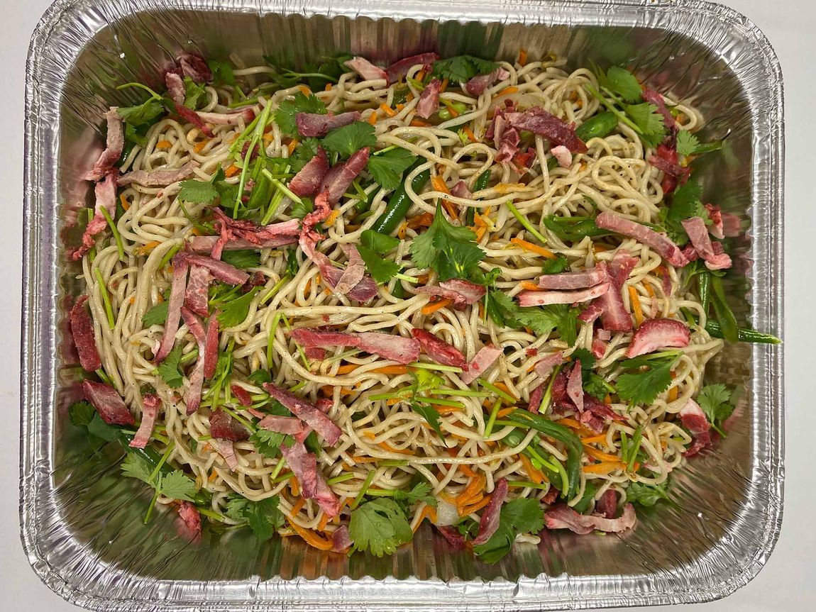 Noodle salad with red pork, cilantro, and shredded vegetables in a foil pan