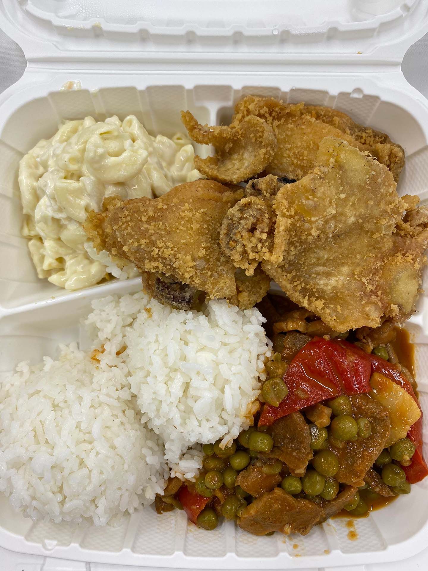A takeout container with fried chicken, macaroni salad, rice, and a vegetable stew
