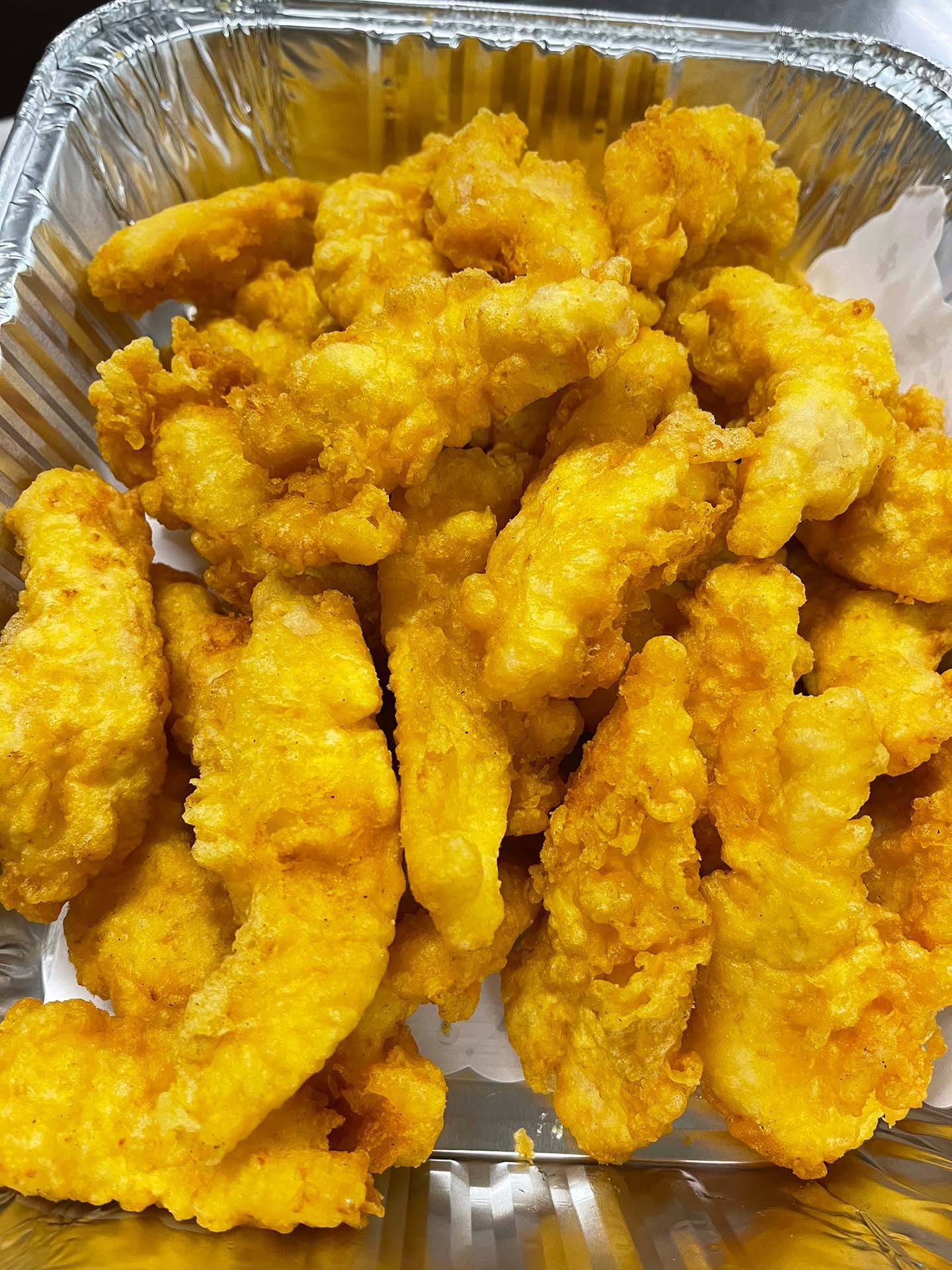 Golden-brown fried chicken tenders in a foil container