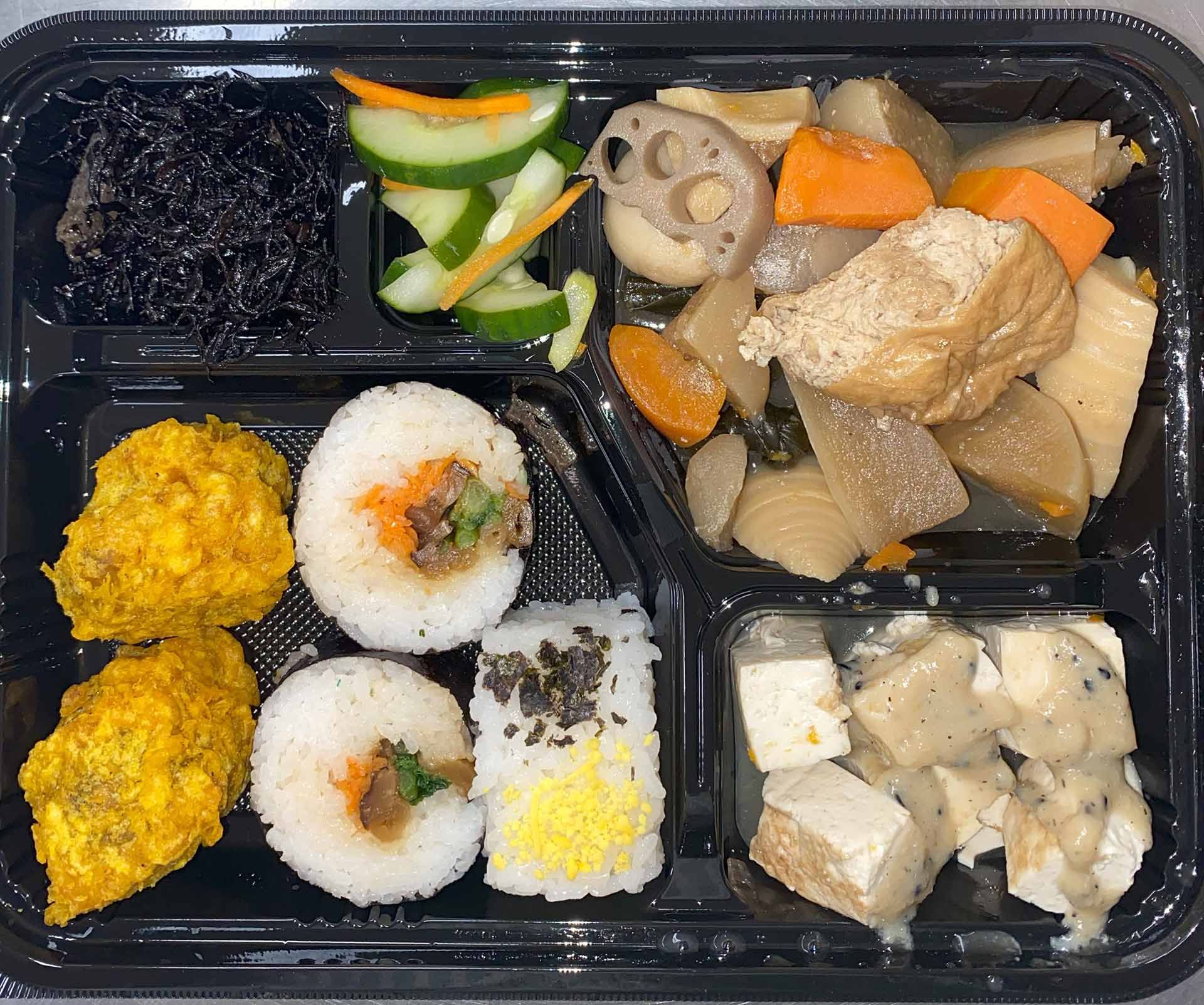 Bento box with various Japanese foods, including sushi rolls, tempura, pickled vegetables, and simmered vegetables