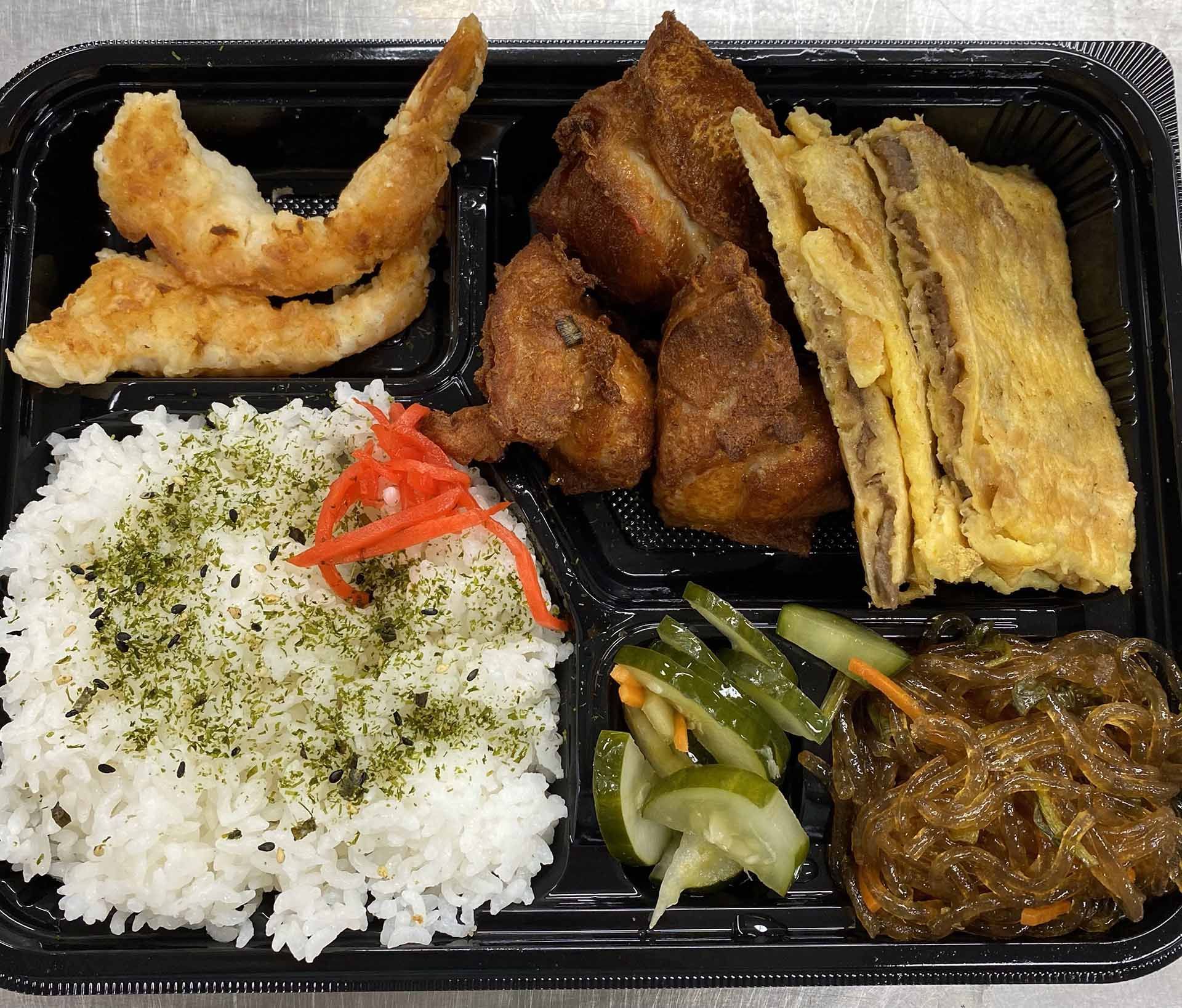 Bento box with rice, fried shrimp, chicken, omelet, pickled cucumbers, and glass noodles