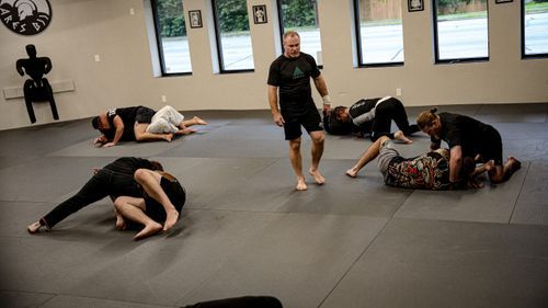 Small group jiu-jitsu training in a bright gym, coach observing as students practice grappling.