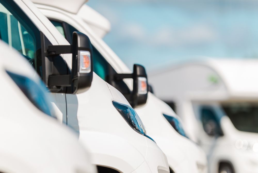 A row of white vans are parked next to each other in a parking lot.