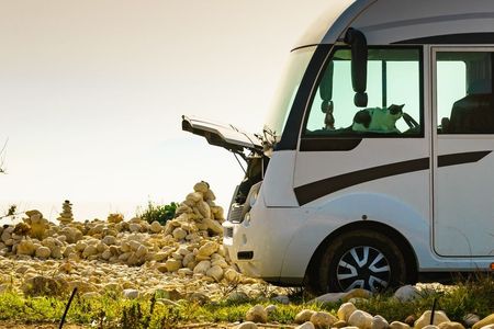 A white rv is parked in a field with its trunk open.