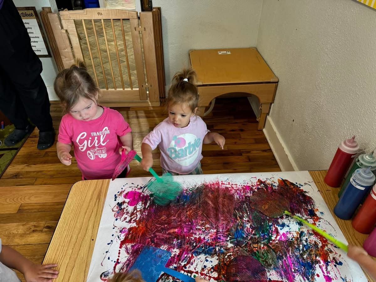 Two little girls are playing with paint on a table.