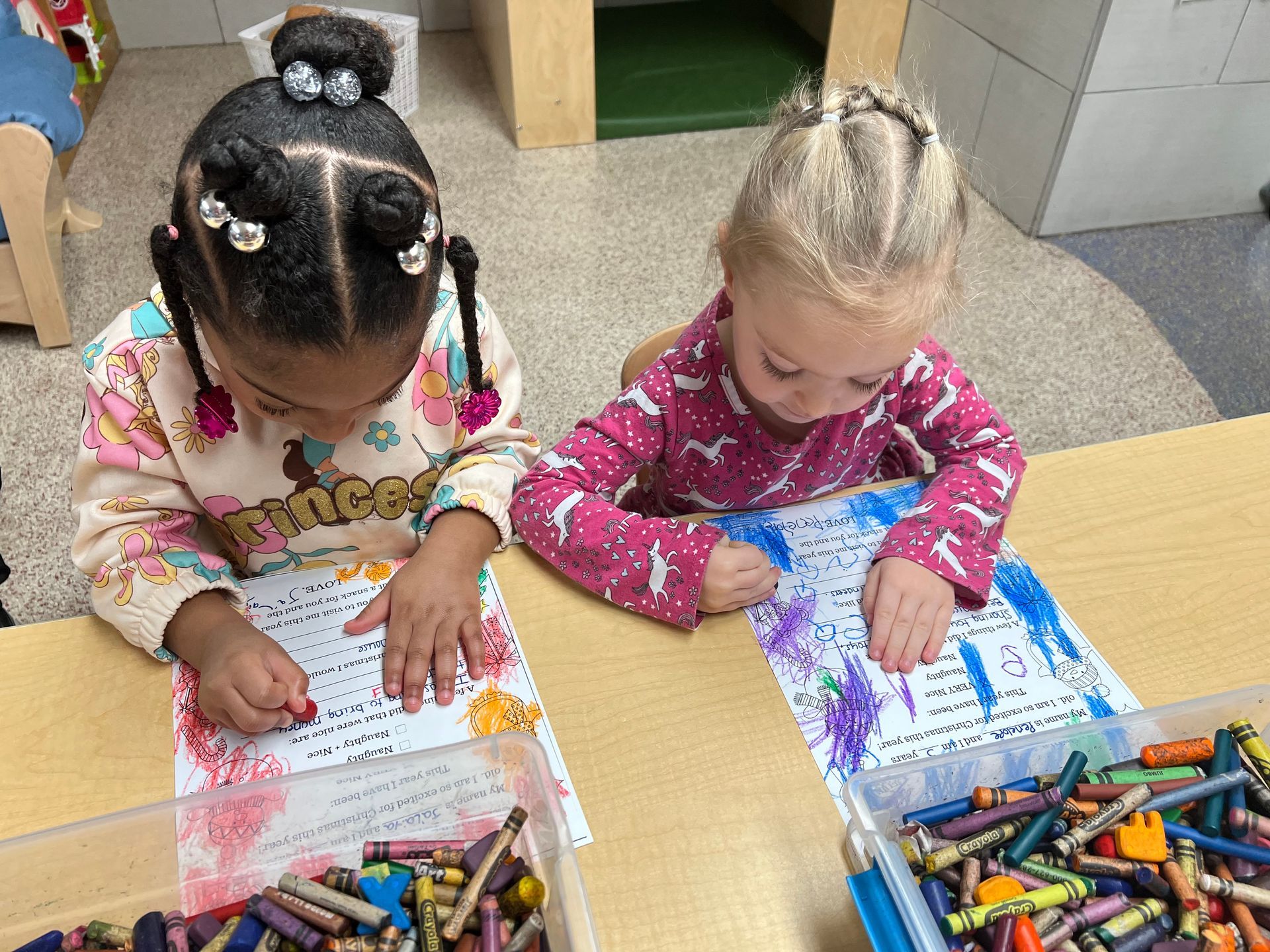 Two little girls are sitting at a table drawing with crayons.