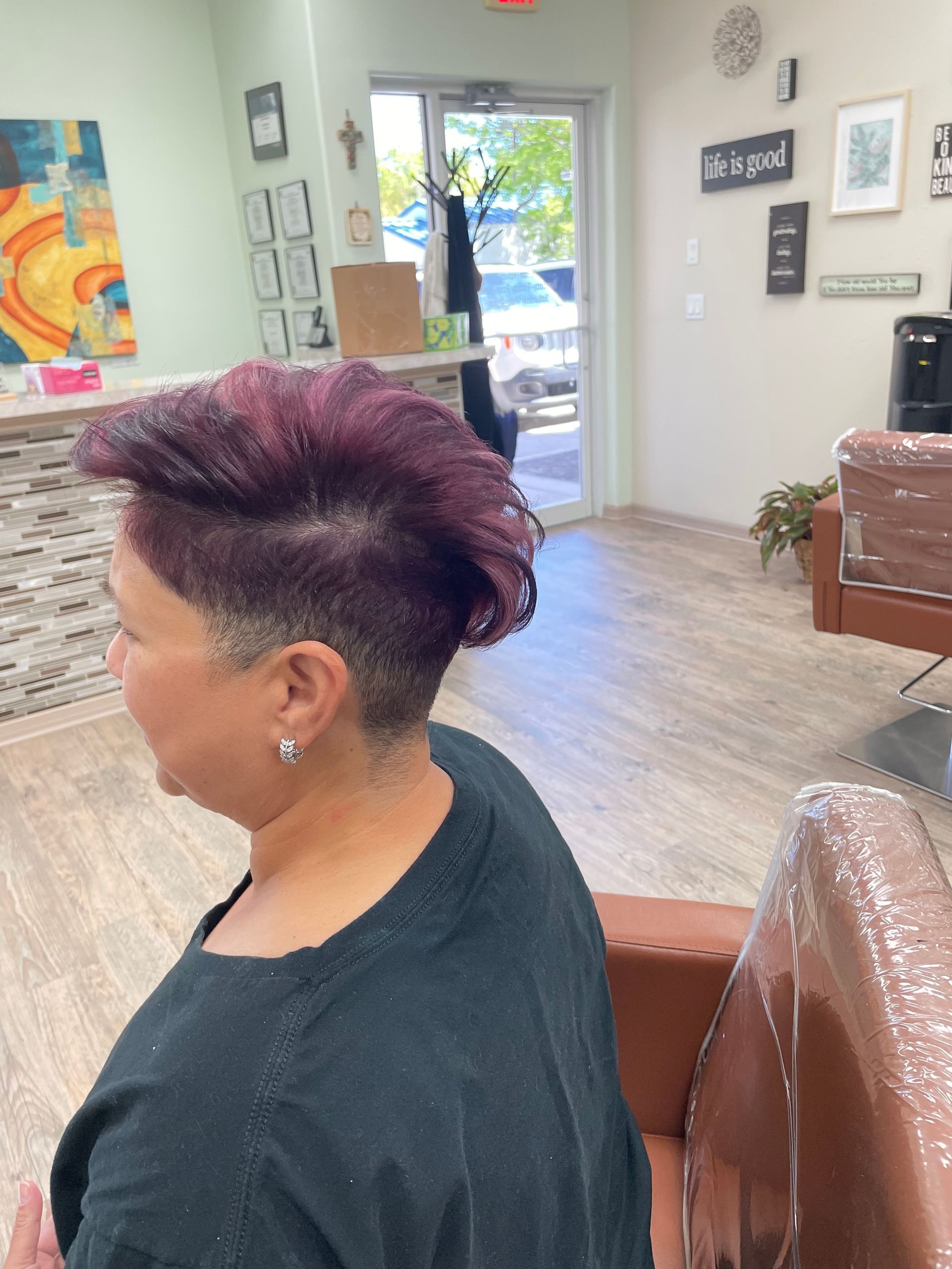 A woman with purple hair is sitting in a chair in a salon.