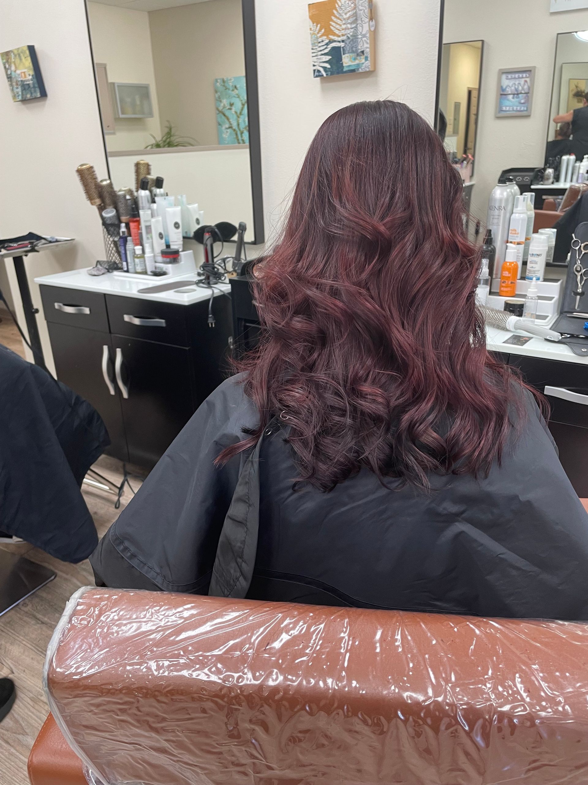 A woman is sitting in a chair in a salon getting her hair cut.