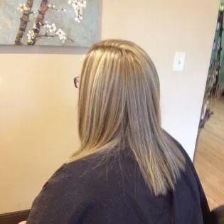A woman with blonde hair and glasses is sitting in front of a painting on the wall