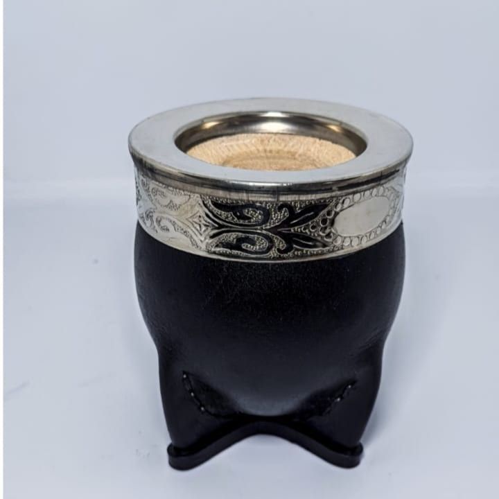 Calabaza negra con borde plateado estampado y tres pequeñas patas sobre un fondo claro.