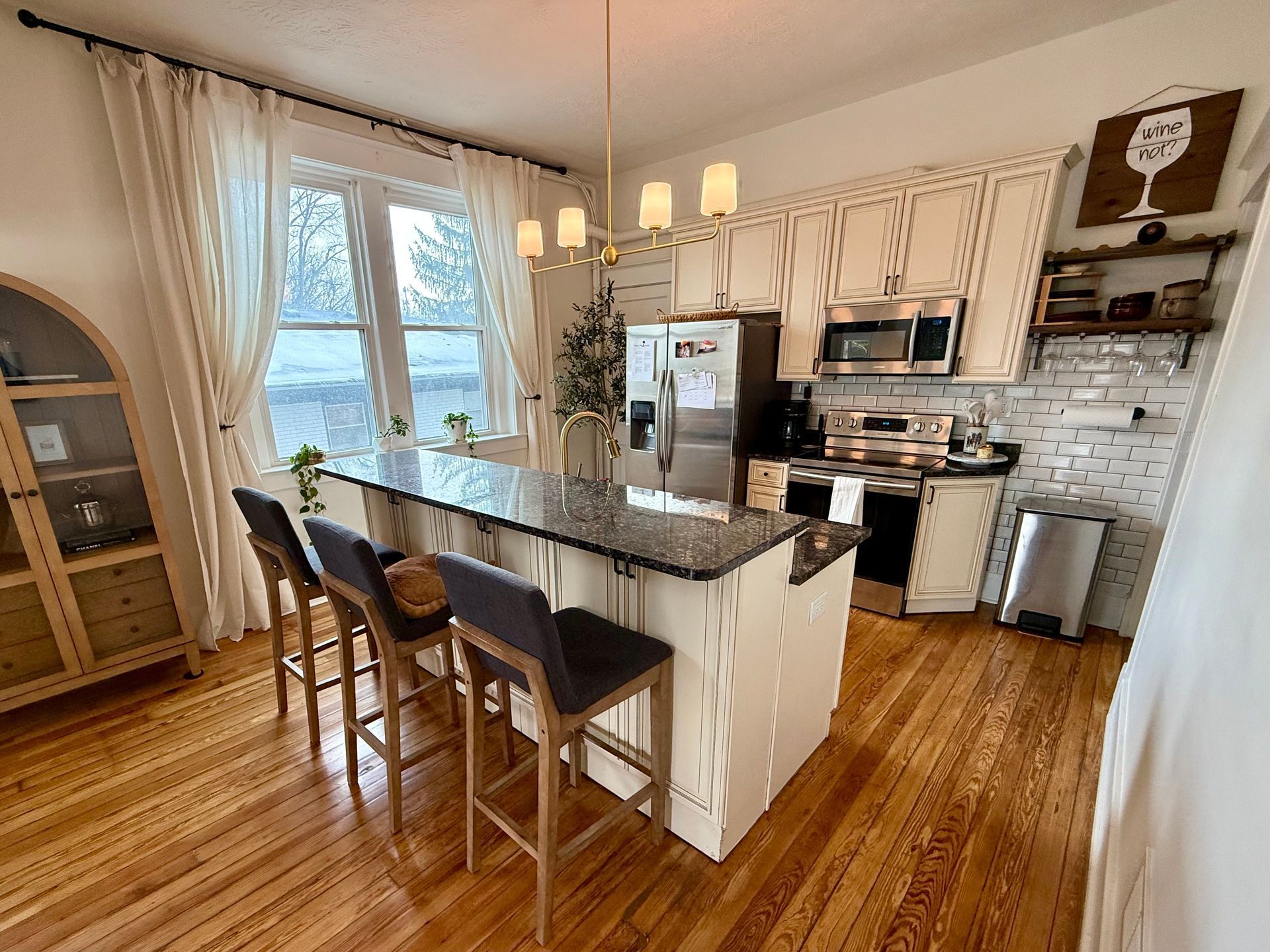 A kitchen with green cabinets , a stove , a microwave , a sink , and a bar.