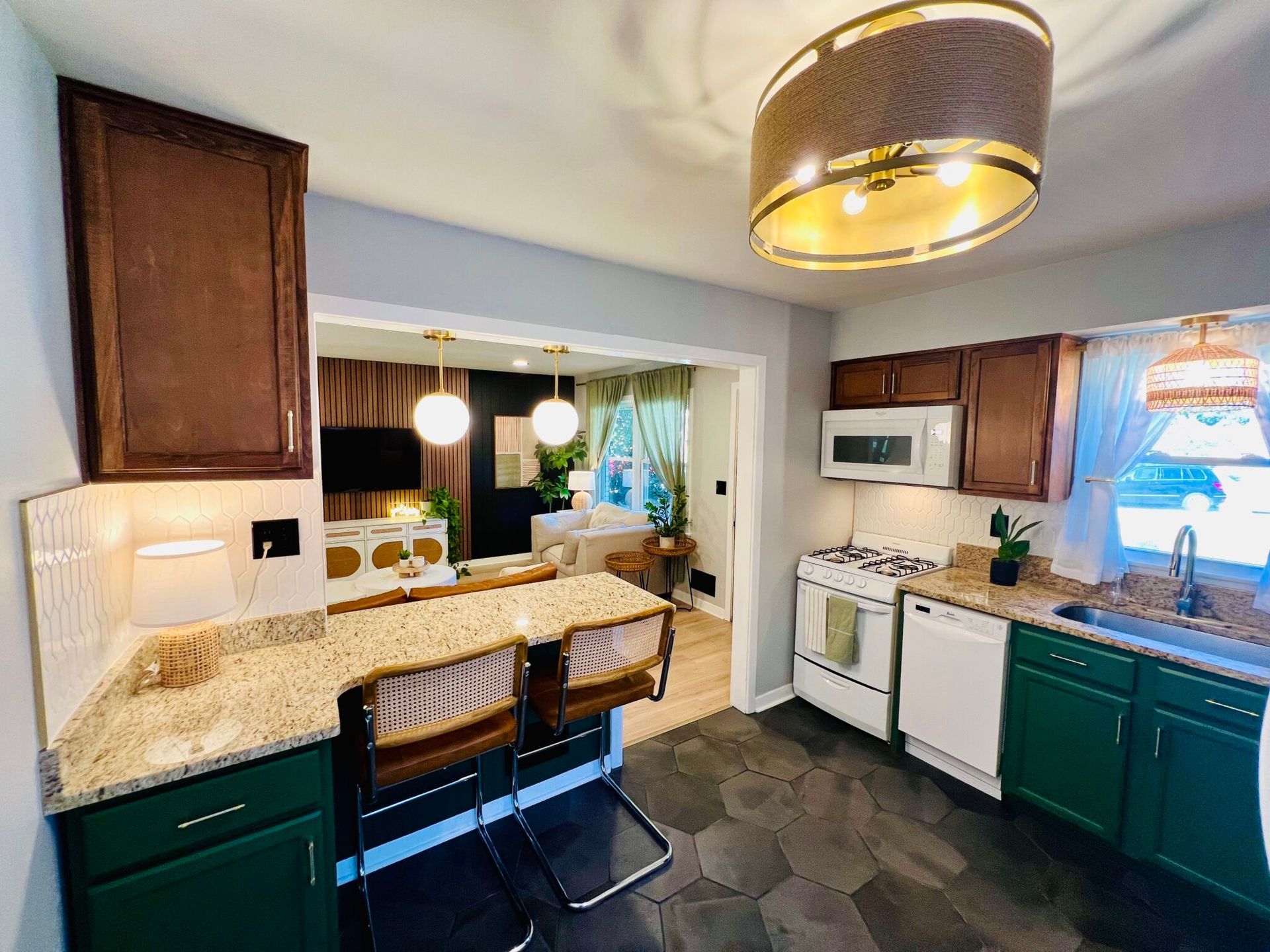 A kitchen with green cabinets , a stove , a microwave , a sink , and a bar.