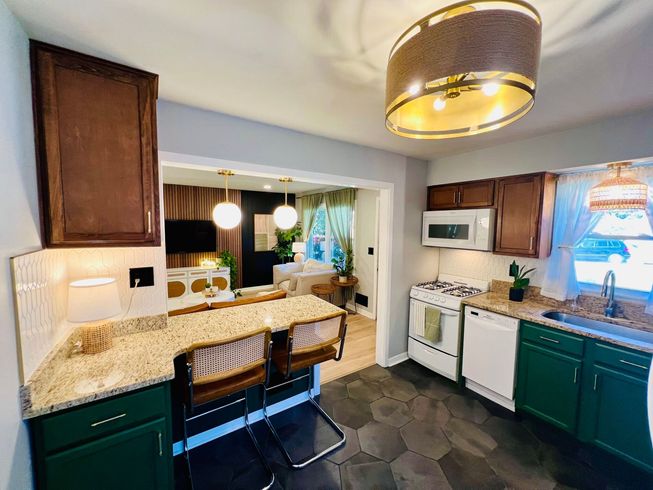 A kitchen with green cabinets , a stove , a microwave , a sink , and a bar.
