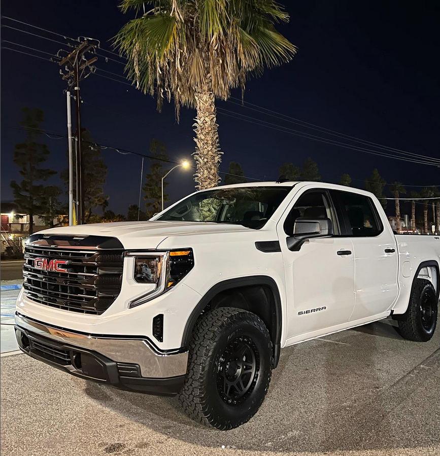 A white gmc truck is parked in front of a palm tree at night.