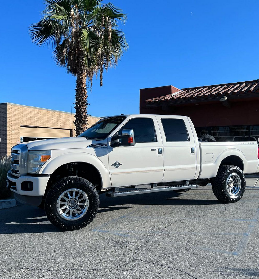 A white truck is parked in front of a building with a palm tree in the background.