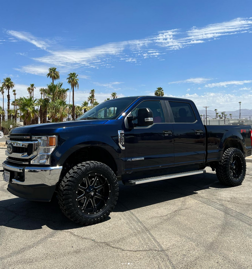 A black pickup truck is parked in a parking lot with palm trees in the background.