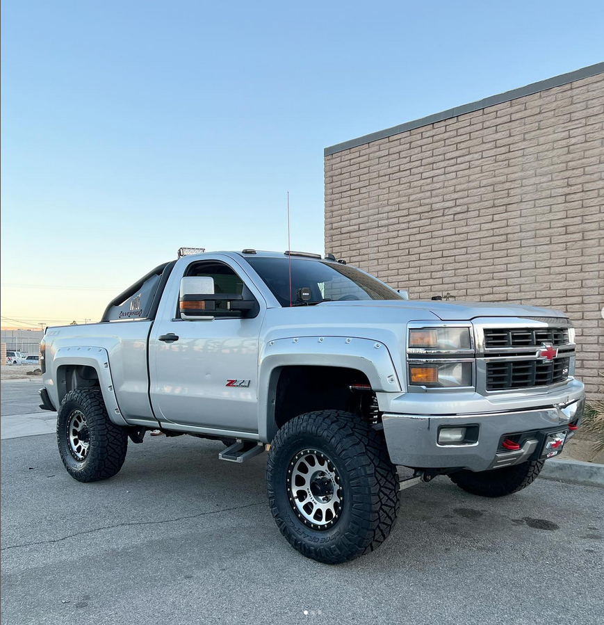 A silver truck is parked in front of a brick building.
