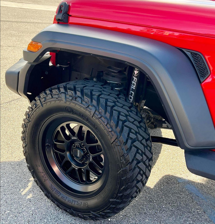 A red jeep with black wheels and tires is parked on the side of the road.