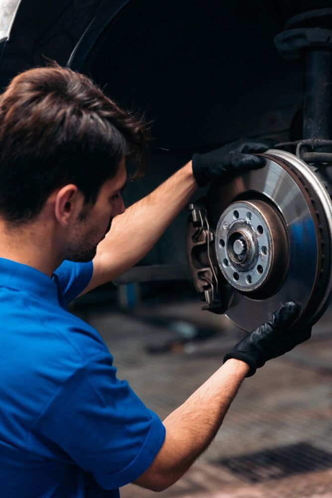 A Man In A Blue Shirt Is Fixing A Brake Disc On A Car — Tonics Automotive in Garbutt, QLD
