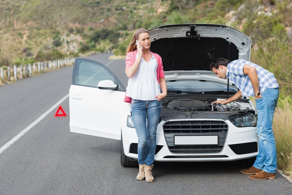 A Man And A Woman Are Standing Next To A Broken Down Car On The Side Of The Road — Tonics Automotive in Garbutt, QLD