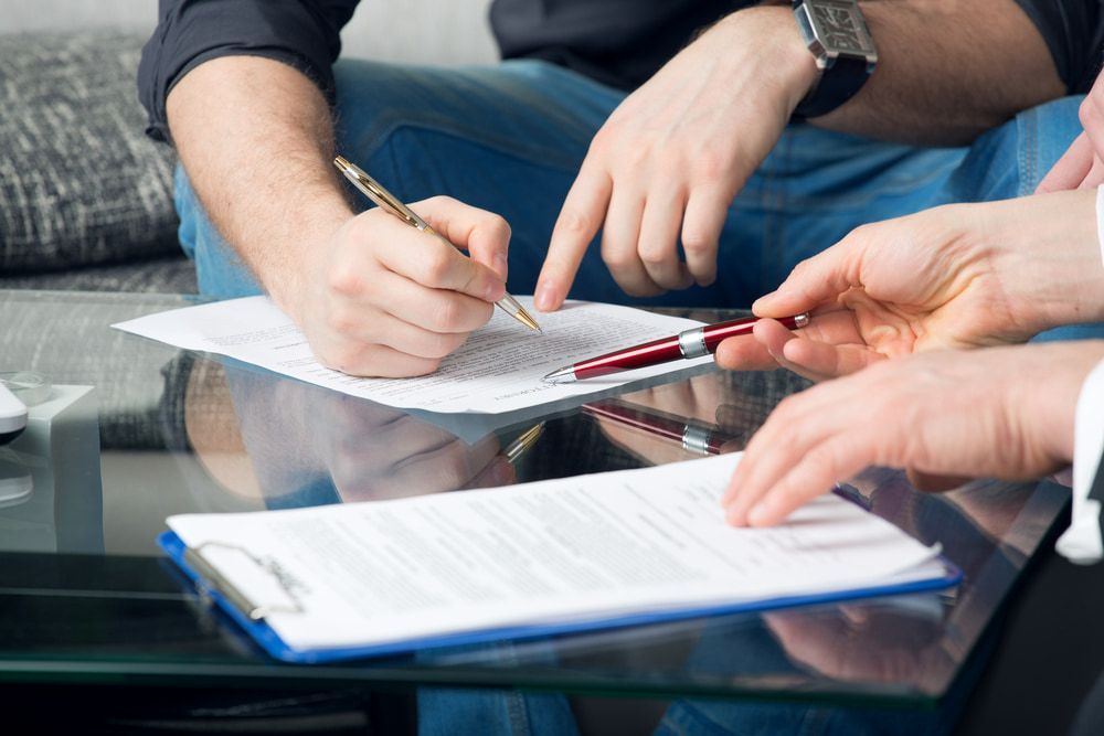 A Group Of People Are Sitting At A Table Signing A Document — Tonics Automotive in Garbutt, QLD