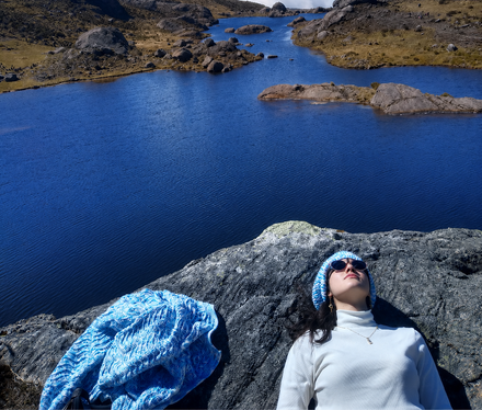 Una persona tumbada sobre una roca junto a un lago de un azul brillante con una manta azul cerca.