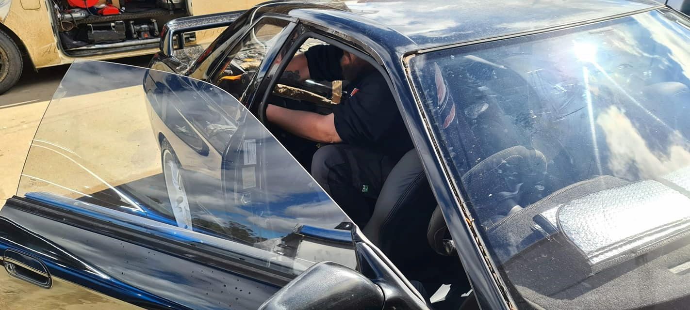 A Man is Sitting in a Car With the Door Open — MJR Auto Glass In Bowral, NSW