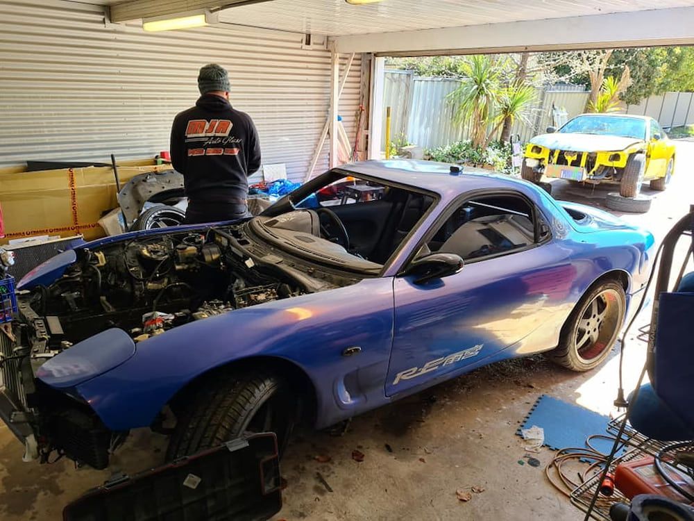A Man is Standing Next to a Blue Sports Car in a Garage — MJR Auto Glass In Moss Vale, NSW