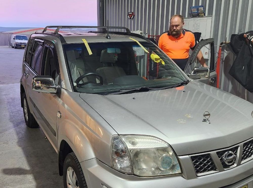 A Man is Standing Next to a Silver Suv in a Garage — MJR Auto Glass In Canberra, ACT