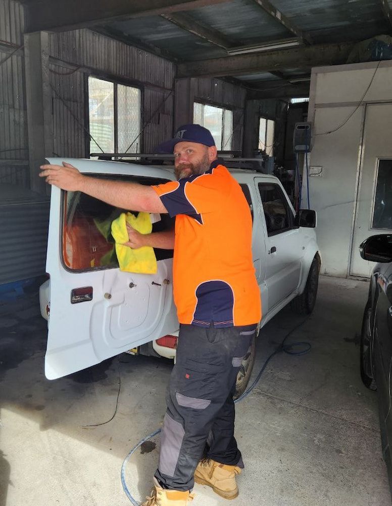 A Man in an Orange Shirt is Cleaning the Windshield of a White Car — MJR Auto Glass In Canberra, ACT