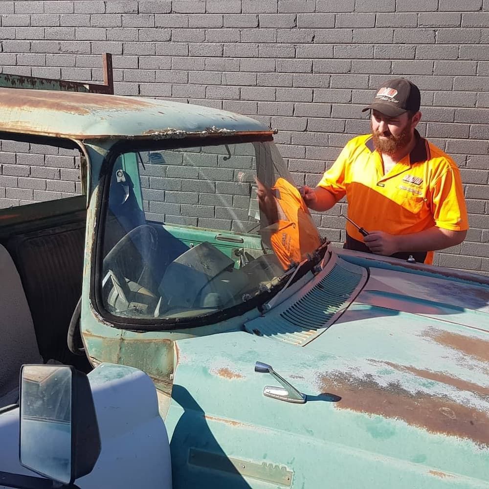 A Man in an Orange Shirt is Cleaning the Windshield of an Old Truck — MJR Auto Glass In Crookwell, NSW