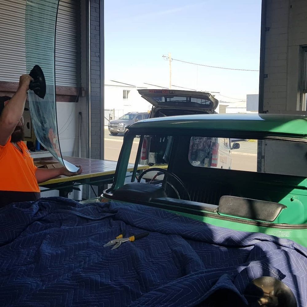 A Man is Installing a Windshield on a Green Car — MJR Auto Glass In Crookwell, NSW