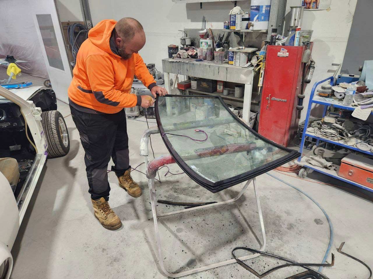 A Man Is Working On A Windshield In A Garage — MJR Auto Glass In Goulburn, NSW