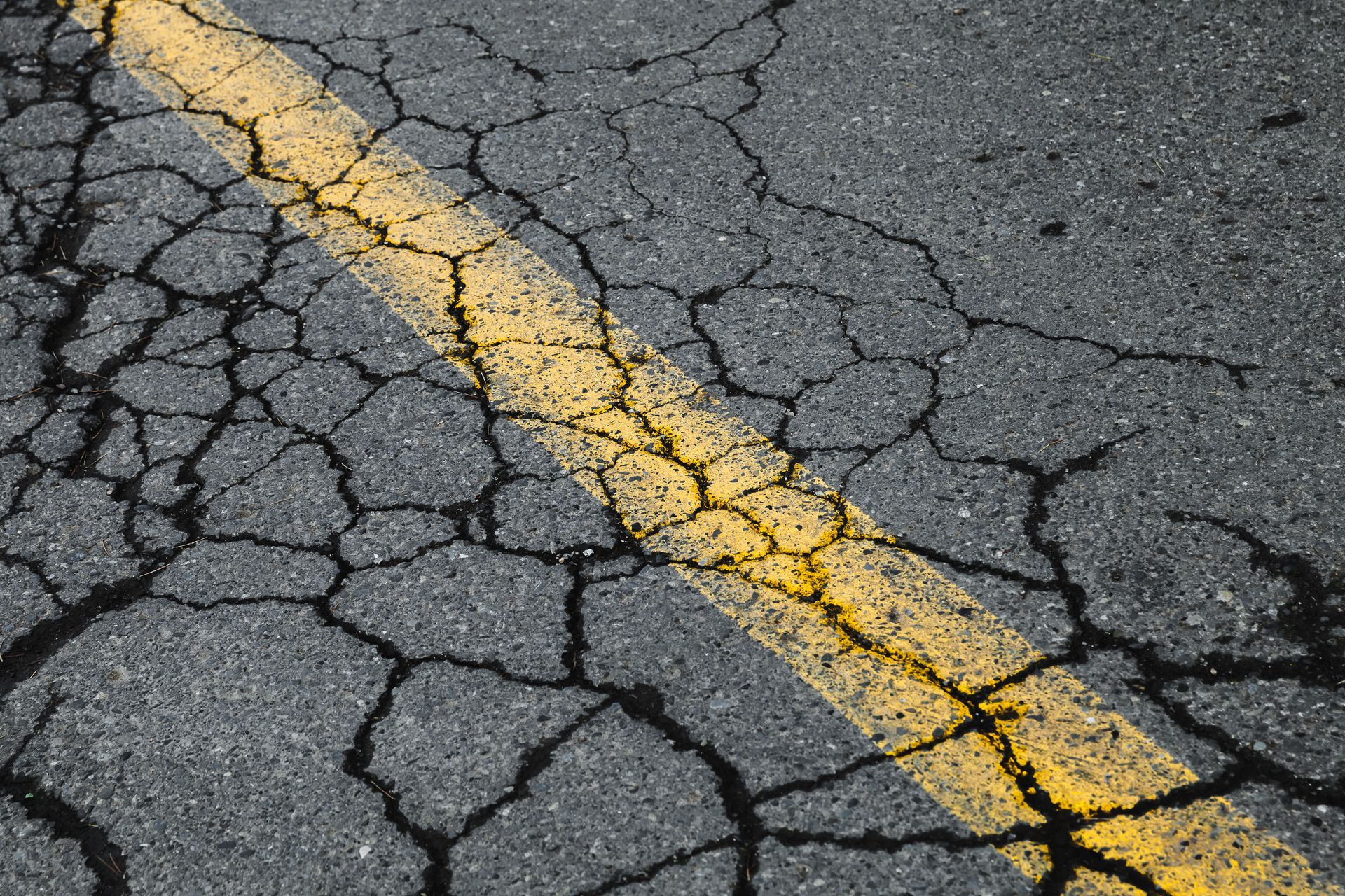 Cracked asphalt in a parking lot running through a yellow divider line.