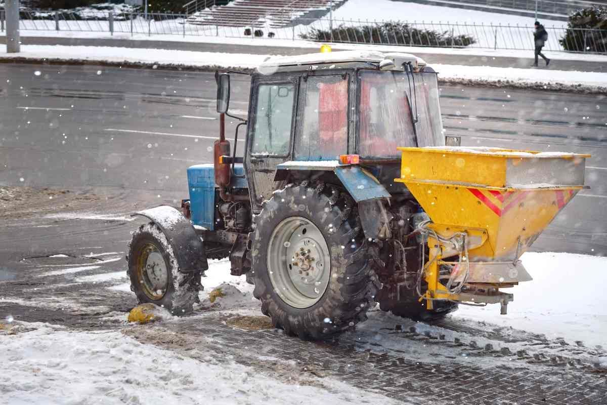 A small tractor spreading salt over a sidewalk and asphalt driveway in Central Kentucky