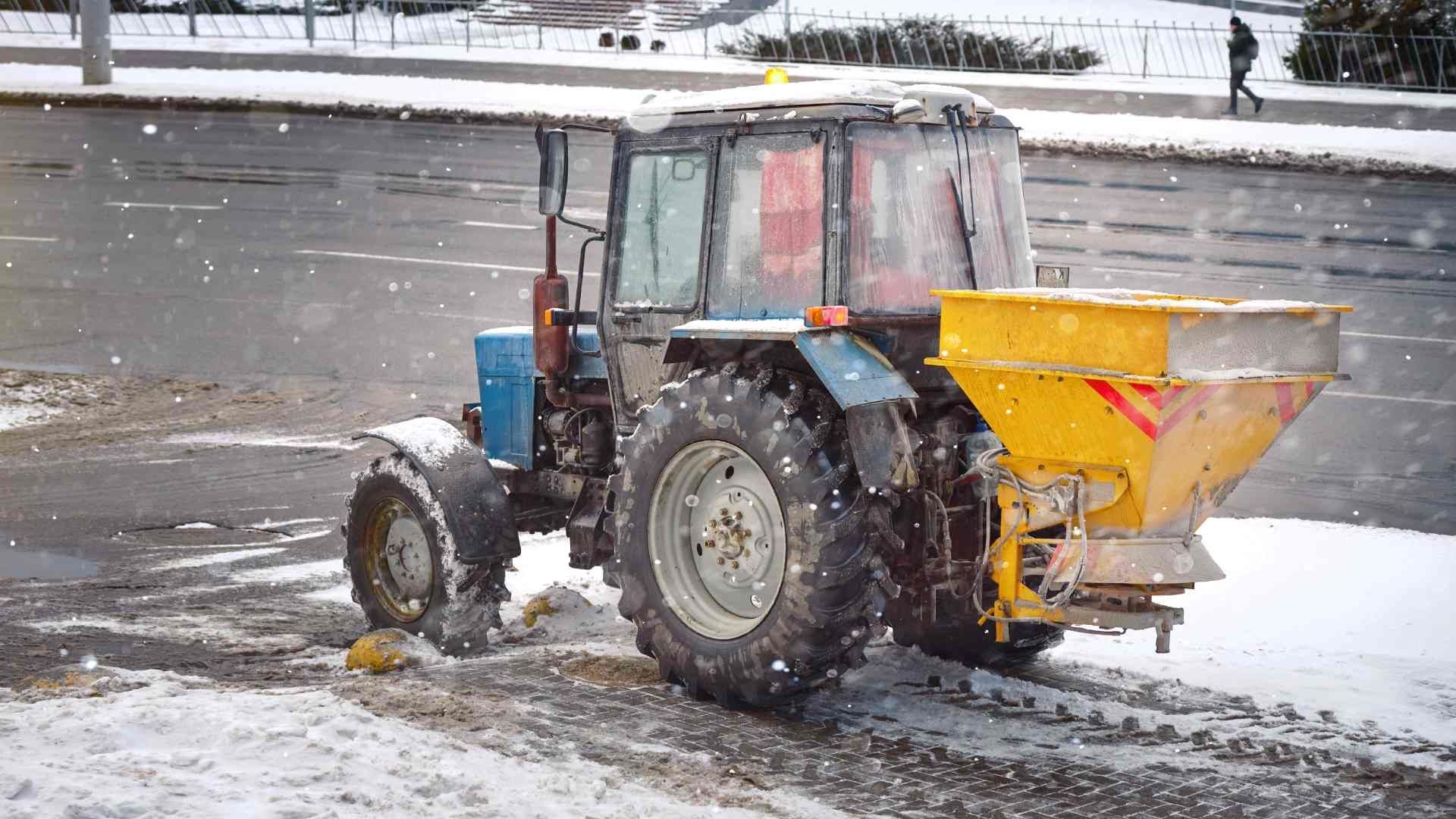 A small tractor spreading salt over a sidewalk and asphalt driveway in Central Kentucky