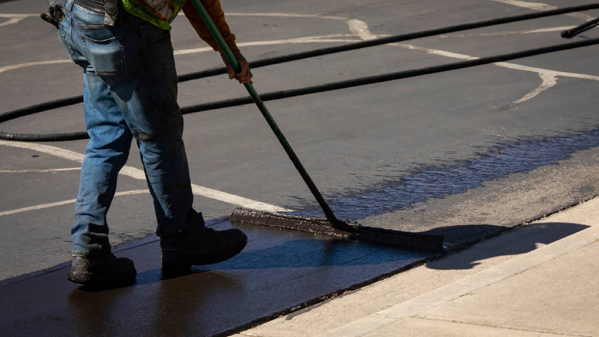 Worker using a sealcoating brush during asphalt resurfacing project near Richmond and Lexington, Ken
