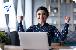 Uma mulher está sentada em frente a um laptop com os braços no ar.