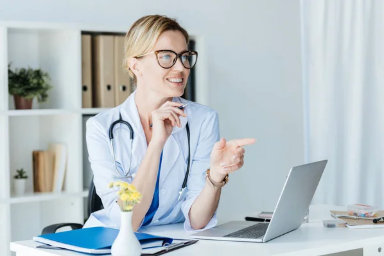 Uma médica está sentada em uma mesa com um laptop.